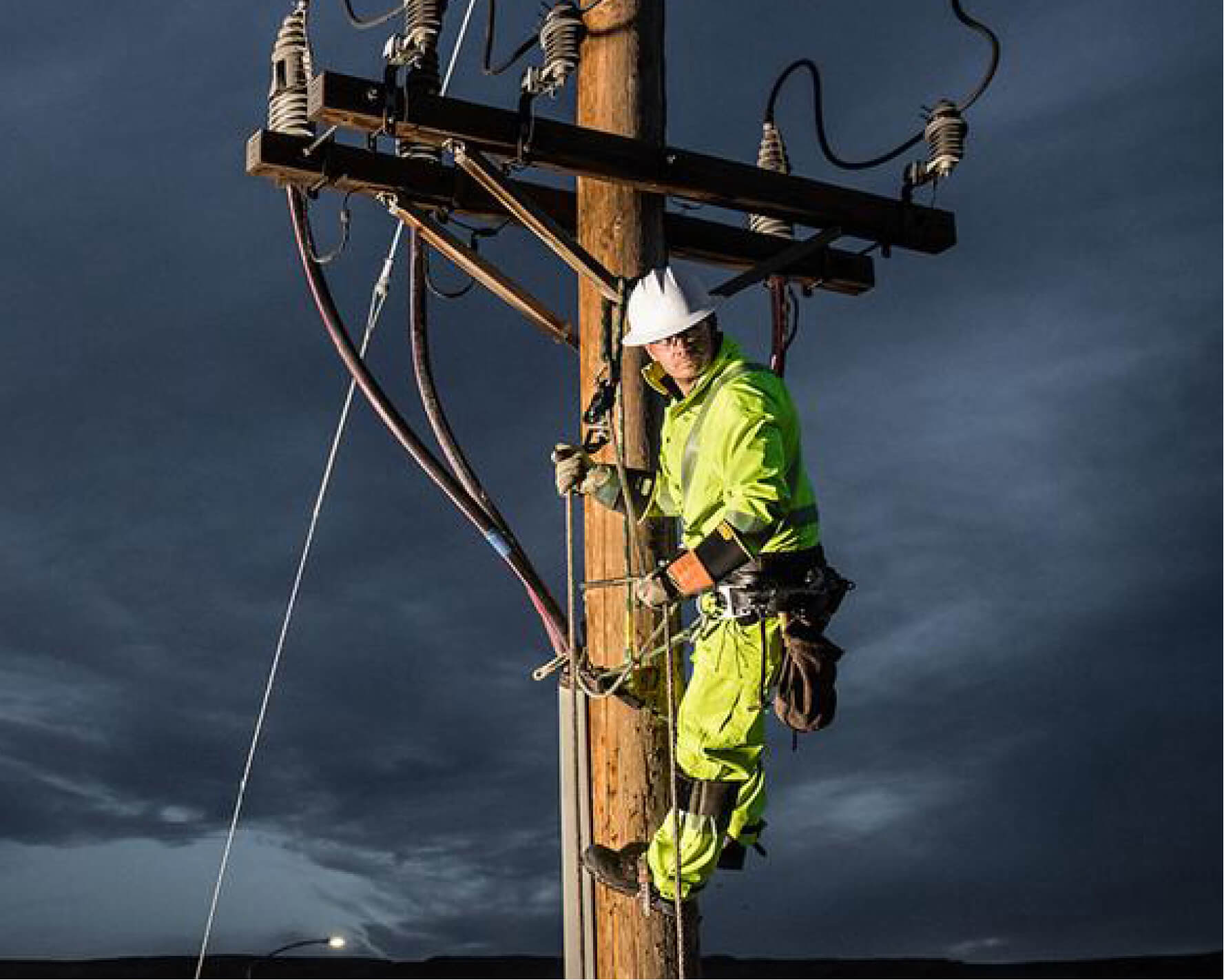 An electrician in Lac Mac protective suit is climbing on an electrical pole.